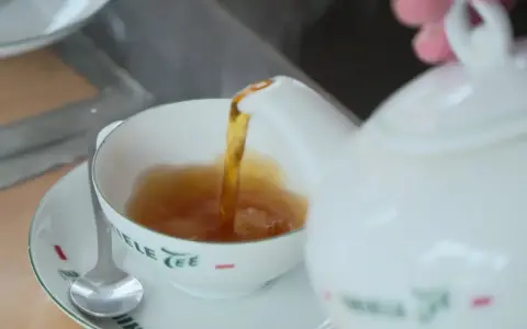 Tee mit Rum norddeutsch: Eine weiße Kanne gießt heißen Tee in eine Tasse. Ein Löffel liegt auf der Untertasse.