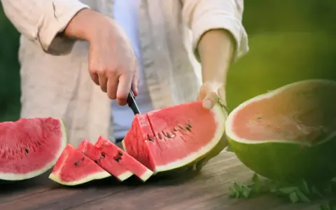 Mężczyzna kroi soczystego arbuza, pokazując, jak wybrać dobrego arbuza. Na stole leżą już pokrojone kawałki.