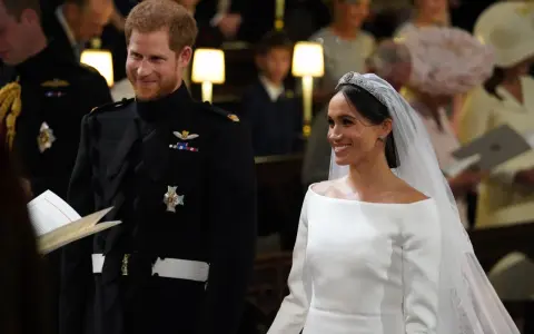 Meghan Markle y el Príncipe Harry sonríen en su boda. Ella luce un vestido blanco y él un uniforme militar.