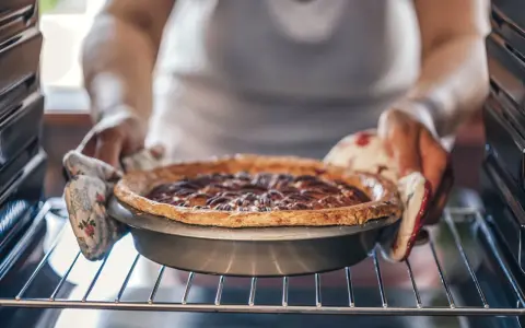 Hände mit Ofenhandschuhen nehmen einen frisch gebackenen Nusskuchen aus dem Ofen. Alles, was man zum Backen braucht: Zutaten, ein Rezept und Geduld.