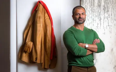 Livio De Marchi, artiste sculpteur, pose à côté de son manteau en bois sculpté, une œuvre saisissante.