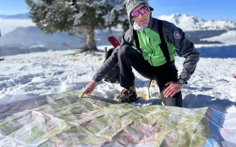 Un homme en tenue de ski pointe une carte sur la neige, planifiant son ascension vers le plus haut sommet de France.