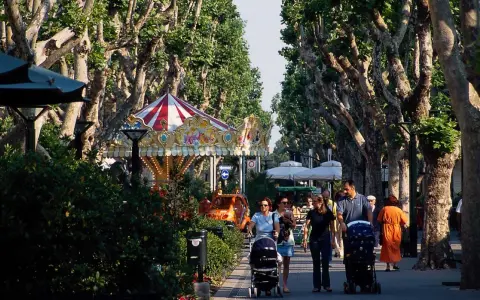 Passeggiata nel centro di Bellaria, con giostra, alberi maestosi e famiglie con passeggini.