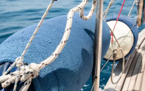 Blauer Fender am Boot befestigen mit Seilen. Das Boot gleitet auf dem blauen Meer.