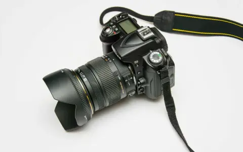 Czarna lustrzanka cyfrowa Nikon z obiektywem i paskiem na białym tle.