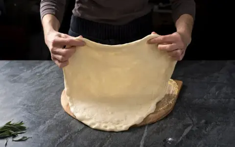 Rozciąganie elastycznego ciasta na pizzę, idealnego do szybkiego przepisu na ciasto do pizzy.