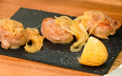 Tiernos medallones de carne al jerez, cubiertos con cebolla caramelizada y acompañados de una porción de patata.