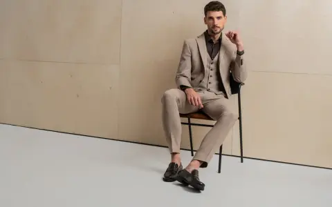 Elegancki mężczyzna w beżowym garniturze, uosabiający włoski styl męski, siedzi na krześle.