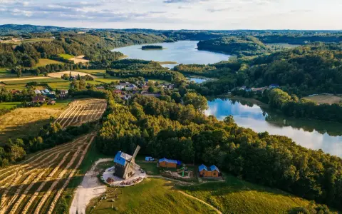 Malowniczy krajobraz kaszub z jeziorem, lasami, polami i drewnianym wiatrakiem.