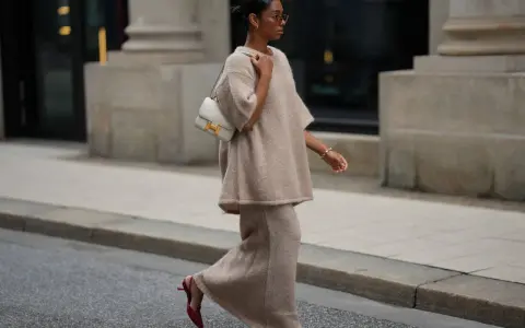 Donna con completo beige e borsa bianca, indossa scarpe rosse con tacco kitten, un dettaglio che aggiunge eleganza.