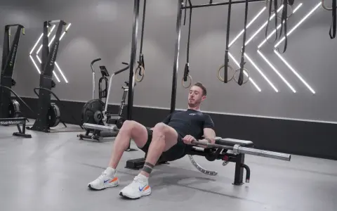 Man utför hip thrust med skivstång på en bänk i ett modernt gym.