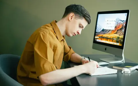 Student pracuje zdalnie, notując pomysły na komputerze. Idealna praca online dla studenta.