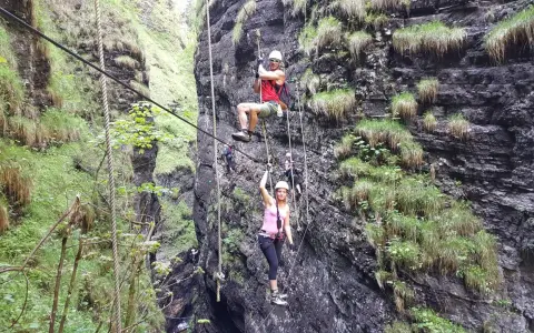 Abenteuer im **Postalmklamm Klettersteig**: Menschen seilen sich durch eine enge Schlucht ab, gesichert an Seilen, umgeben von steilen, bewachsenen Felswänden.