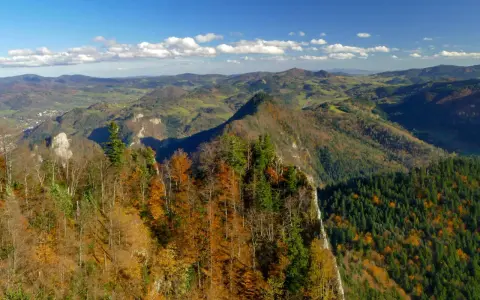 Jesień na szlaku Trzy Korony z Sromowiec Niżnych. Kolorowe drzewa na zboczu gór, w dole dolina i miasteczko.