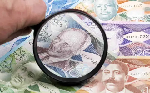 Förstoringsglas granskar sedlar med porträtt, visar Barbados valuta.