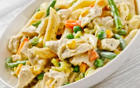 Penne z kurczakiem w kremowym sosie, z groszkiem, marchewką i fasolką szparagową. Pyszne danie obiadowe.