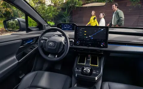 Wnętrze Toyoty bZ4X z ekranem nawigacji. Rodzina na zewnątrz, zastanawia się nad ceną i możliwościami tego elektrycznego SUV-a.