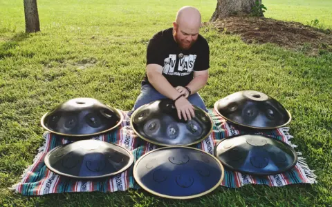 Mann spielt auf mehreren runden Metallinstrumenten im Freien.
