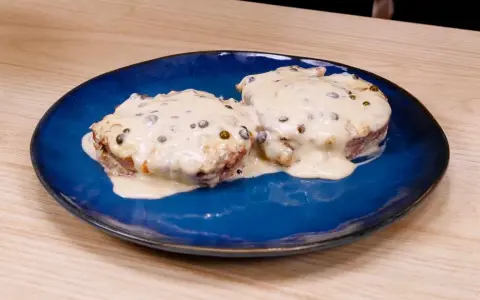 Due medaglioni di filetto al pepe verde, immersi in una cremosa salsa bianca, serviti su un piatto blu.