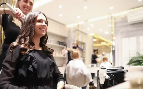 Friseurin stylt lächelnde Kundin mit Lockenstab in modernem Salon.