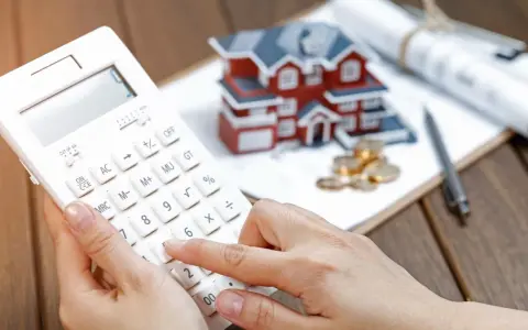 Calculando la casilla 435 renta: una mano usa una calculadora blanca junto a una maqueta de casa, monedas y planos.