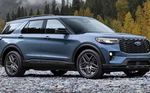 Niebieski Ford Explorer ST zaparkowany na kamienistej plaży, z jesiennym lasem w tle.