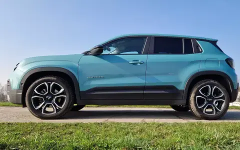 Turkusowy Jeep Avenger 4x4 z czarnymi felgami na tle nieba i trawy.