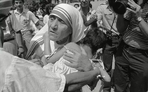Missionaries of Charity founder, Mother Teresa, cradles a child amidst a crowd and media attention.