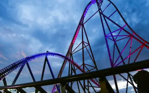 Najwyższy rollercoaster na świecie, oświetlony niebieskim i różowym światłem, wznosi się na tle burzowego nieba.