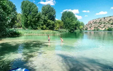 Dos niños disfrutan de las piscinas naturales de Albacete, con aguas cristalinas y rodeadas de vegetación exuberante.