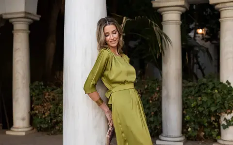 Una mujer con un vestido verde oliva satinado, como una de las madrinas elegantísimas, posa apoyada en una columna de mármol.