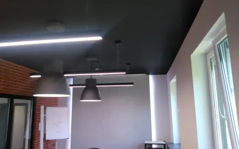 Nowoczesne biuro z czarnym sufitem (RAL 9004), wiszącymi lampami i ceglaną ścianą.