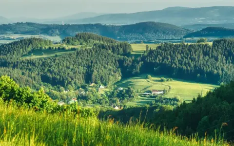 Zielone wzgórza i lasy Gór Sowich, z widocznymi domami i polami. Idealne miejsce na odkrywanie atrakcji i odpoczynek na łonie natury.