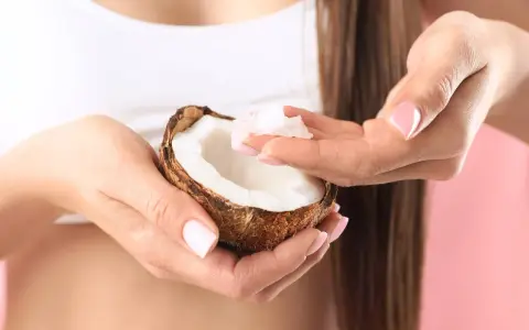 Mani con unghie curate prendono polpa di cocco da una noce, ingrediente perfetto per una maschera capelli fai da te nutriente.