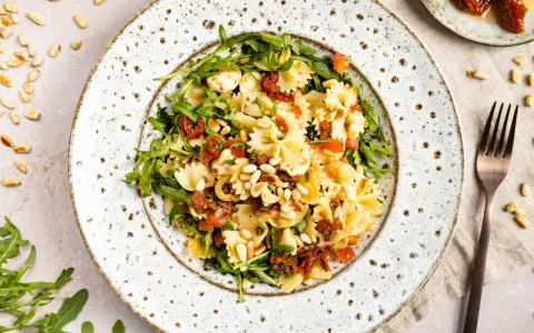 Ein köstlicher mediterraner Salat mit Farfalle, getrockneten Tomaten, Rucola und Pinienkernen.