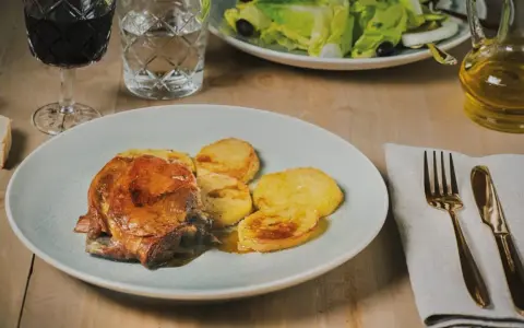 Plato de carne asada con patatas, un ejemplo de comida típica de Huesca. Acompañado de ensalada, vino tinto y aceite de oliva.