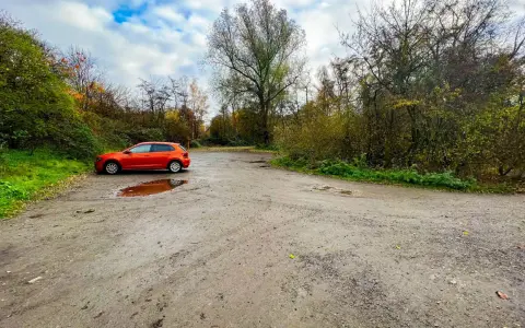 Ein orangefarbener VW Polo parkt auf einem matschigen Parkplatz am Rande eines Waldes. Die Halde Haniel Parken ist von Bäumen und Herbstlaub umgeben.