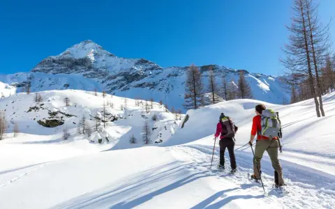 Coppia con ciaspole esplora un sentiero innevato in montagna, un'ottima idea per chi cerca dove ciaspolare in Lombardia.