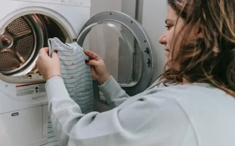 Mujer revisa una prenda antes de meterla a la secadora, pensando en como hacer que encoja la ropa.