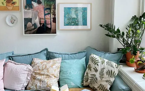 Acogedor rincón de plantas en el salón, con un sofá azul, cojines decorativos y cuadros en la pared.