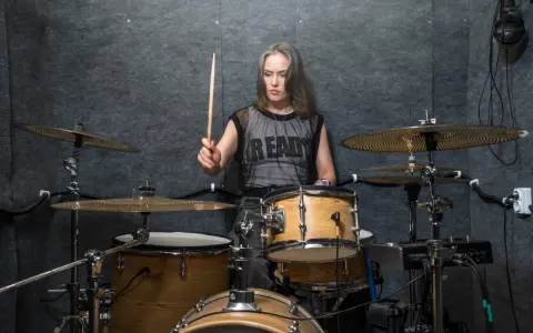 Kobieta z pałeczką w dłoni, gotowa do wygenerowania mocnych **drum beats** na zestawie perkusyjnym w studio.