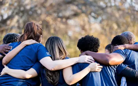 A diverse group of people in blue shirts huddle together, arms around each other, symbolizing collaboration and the strength of revenue diversification.