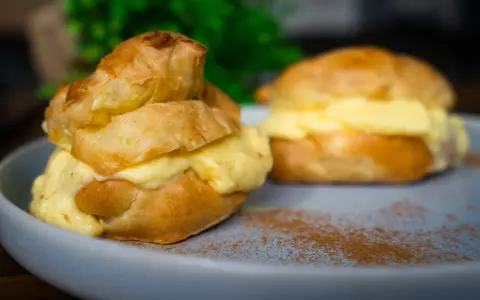 Zwei köstliche Windbeutel-Desserts, gefüllt mit cremiger Vanillecreme, auf einem Teller mit Zimt bestäubt.