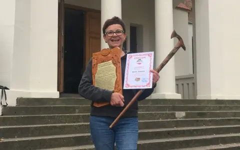 Uśmiechnięta kobieta z dyplomem i drewnianą laską, zdobywczyni Korony Gór Polskich.