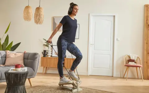 Une femme fait du step à la maison, casque sur les oreilles, pour un entraînement cardio efficace dans son salon.