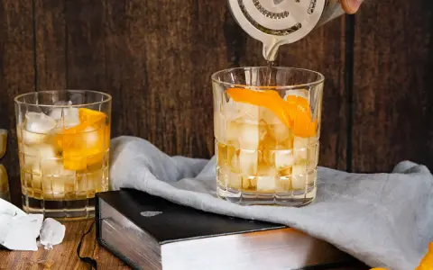 Ein Old Fashioned wird zubereitet, Eiswürfel und Orangenschale zieren das Glas. Ein altes Rezept wird lebendig.