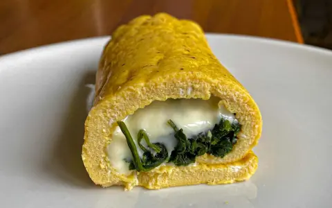 Rotolo di frittata dorato, ripieno di spinaci e formaggio filante, servito su un piatto bianco.