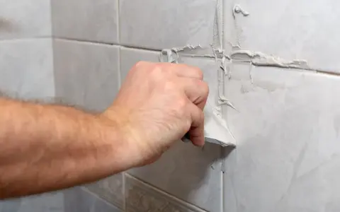 Main d'une personne appliquant du mastic sur les joints d'une salle de bain.