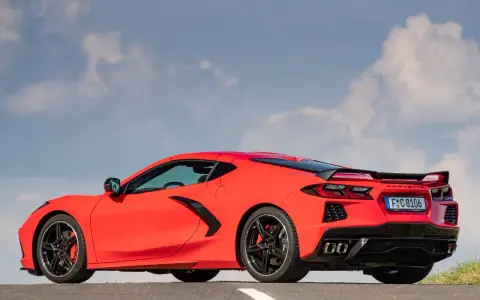 Czerwony Chevrolet Corvette C8 z czarnym spoilerem i felgami, zaparkowany na drodze pod błękitnym niebem z chmurami.
