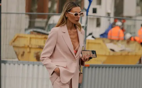 Donna con tailleur rosa, reggiseno a vista e occhiali da sole. Un look chic per ogni occasione.